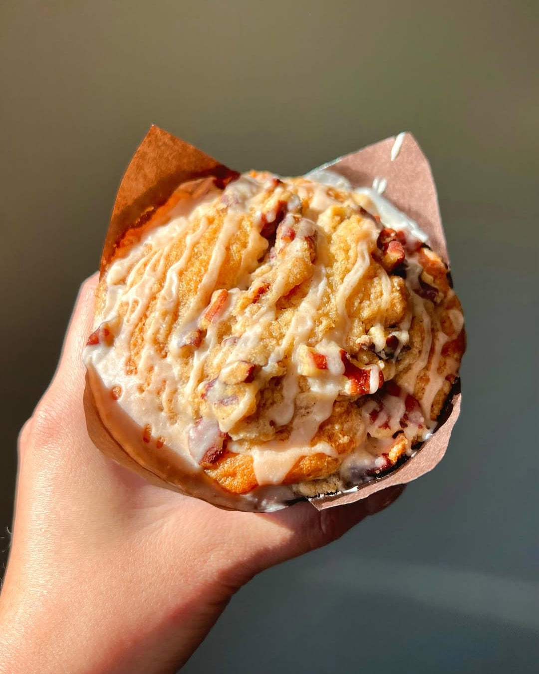 Hand holding a Cinnamon Maple Crumble Muffins with a light glaze against a neutral background