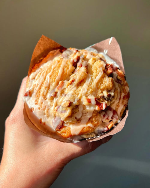 Hand holding a Cinnamon Maple Crumble Muffins with a light glaze against a neutral background