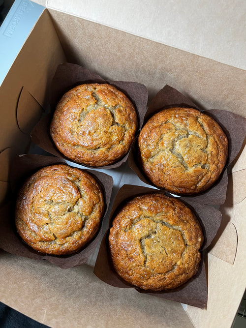 Four muffins in brown paper cups on a cardboard box