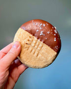 Hand holding a Peanut Butter Cookie with chocolate-dipped half and crisscross pattern and seasalt