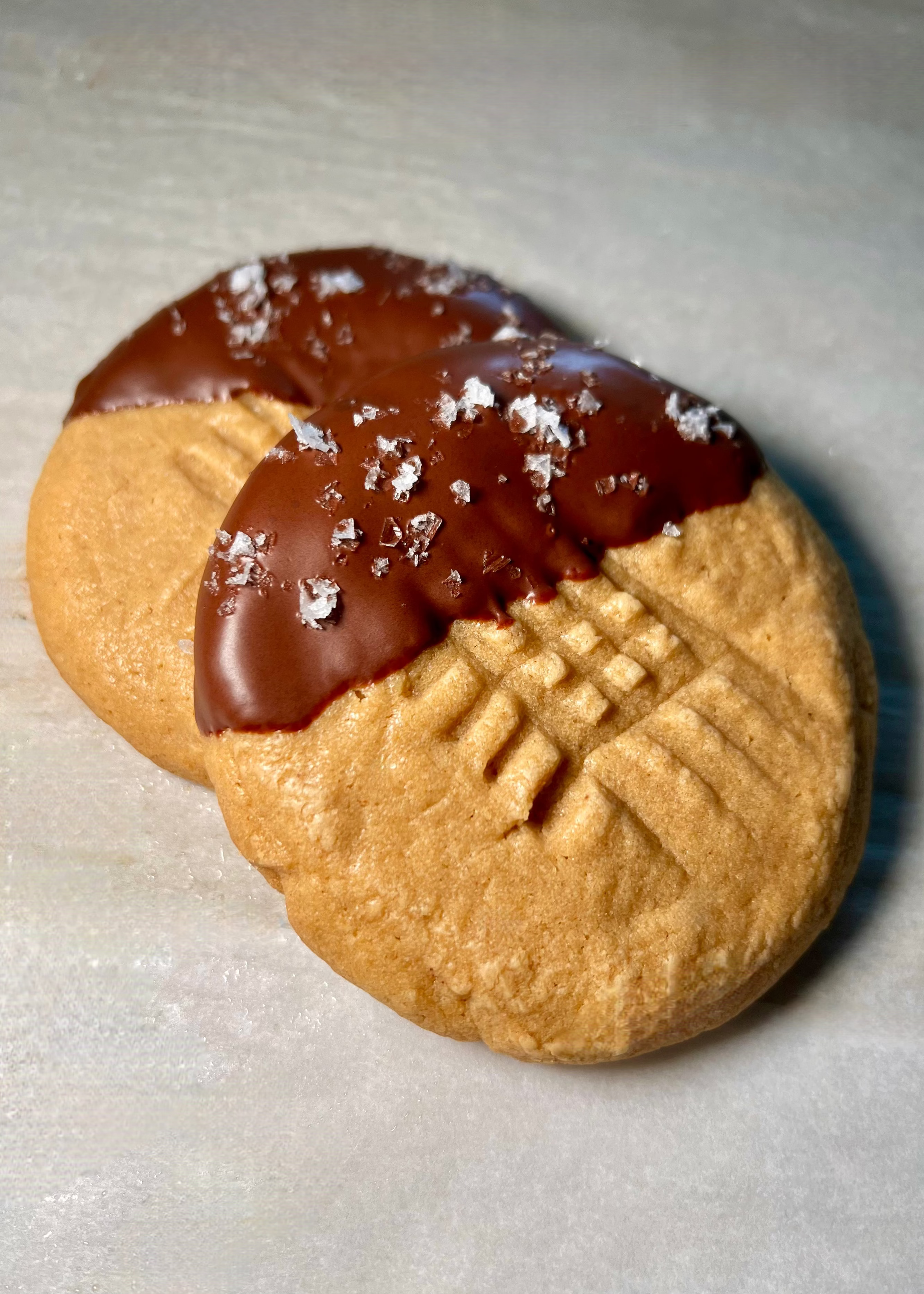 Two peanut butter cookies with chocolate on a light gray background