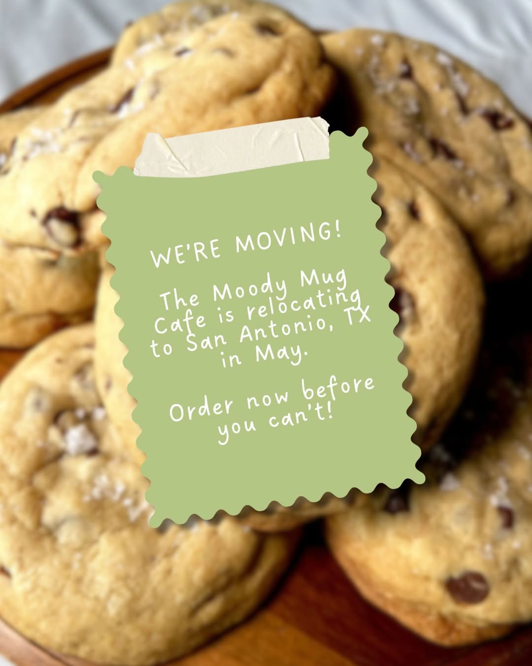 Cookies with a green sign announcing the Moody Mug Cafe's relocation to San Antonio, TX.